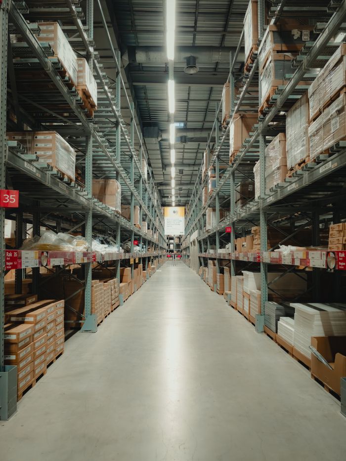 services-03 Spacious warehouse aisle with shelves filled with neatly stacked products and pallets.