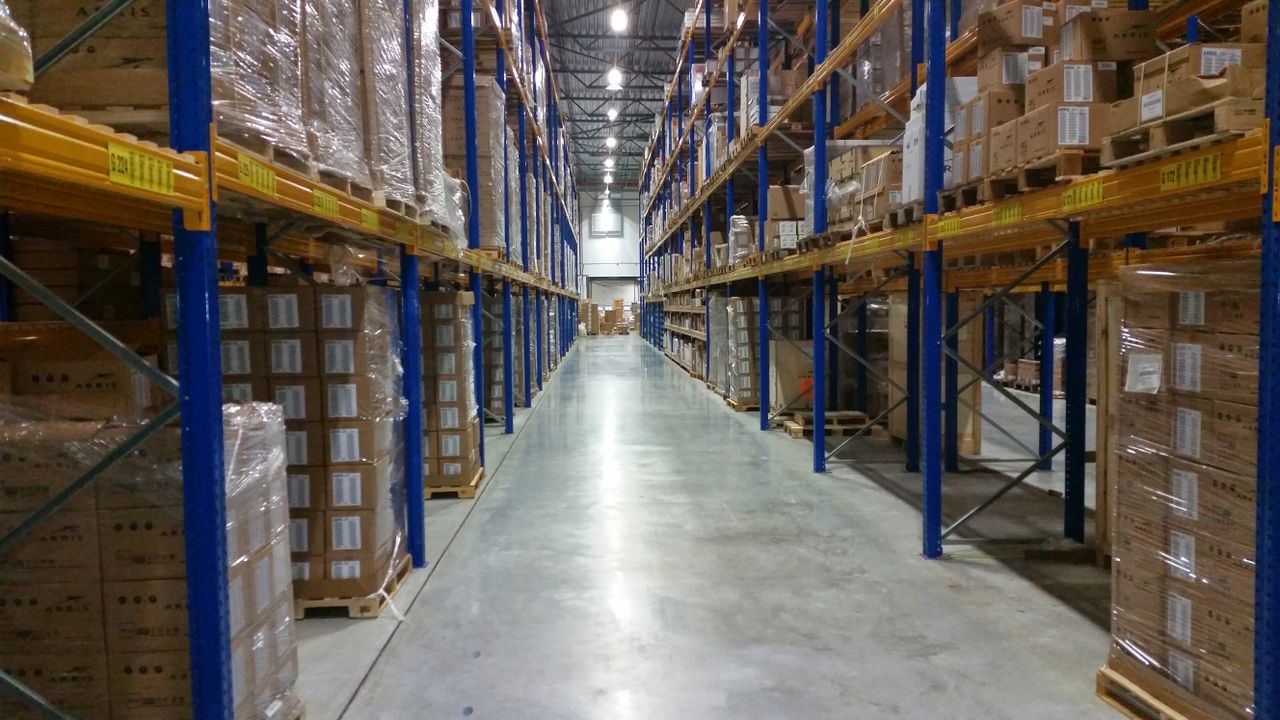 services-01 Interior view of a large warehouse aisle lined with stacks of organized cardboard boxes.